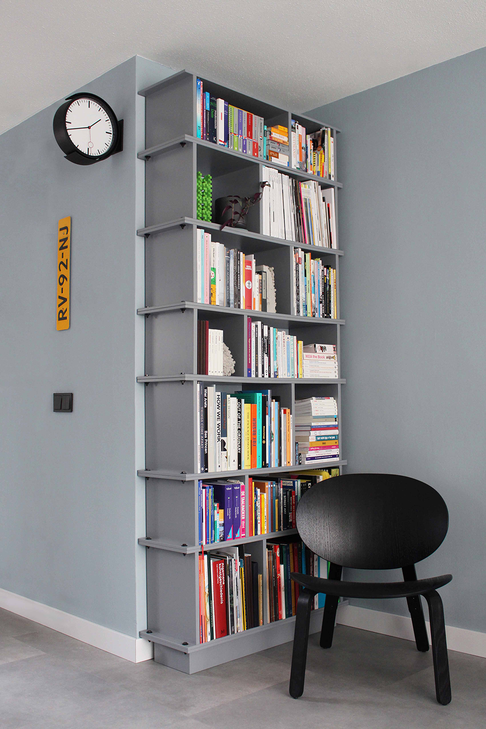Grijze geschilderde boekenkast, bestaande uit losse delen. Met elkaar verbonden door grote zwarte bouten. Interieurontwerp, meubel, meubelmaker, retail design, interior